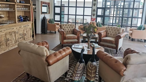 A spacious living room with leather armchairs, a wooden cabinet with glassware, and large windows providing natural light. - The Rez Guesthouse (Walvis Bay)