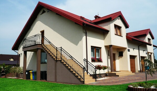 A two-story house with a red roof, a staircase with black railings, and a small garden area.