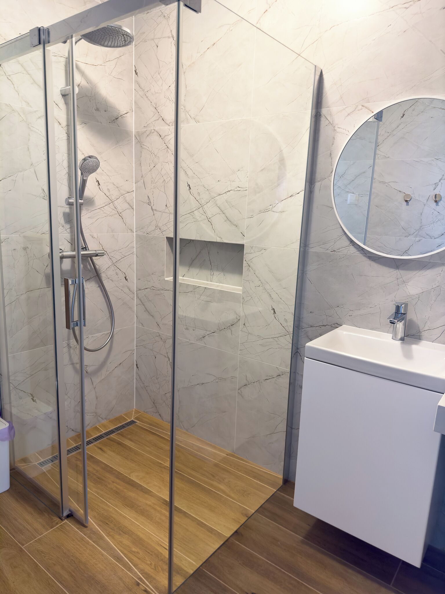 A modern bathroom with a glass-enclosed shower, a white sink, and a marble-tiled wall.