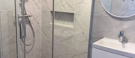A modern bathroom with a glass-enclosed shower, a white sink, and a marble-tiled wall.