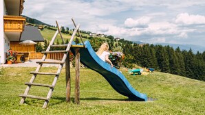 A child on a blue slide in a grassy area with a wooden ladder nearby. - Residence Speckerhof (Rio di Pusteria)
