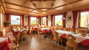 A restaurant with wooden interior, red curtains, and multiple tables and chairs. - Residence Speckerhof (Rio di Pusteria)