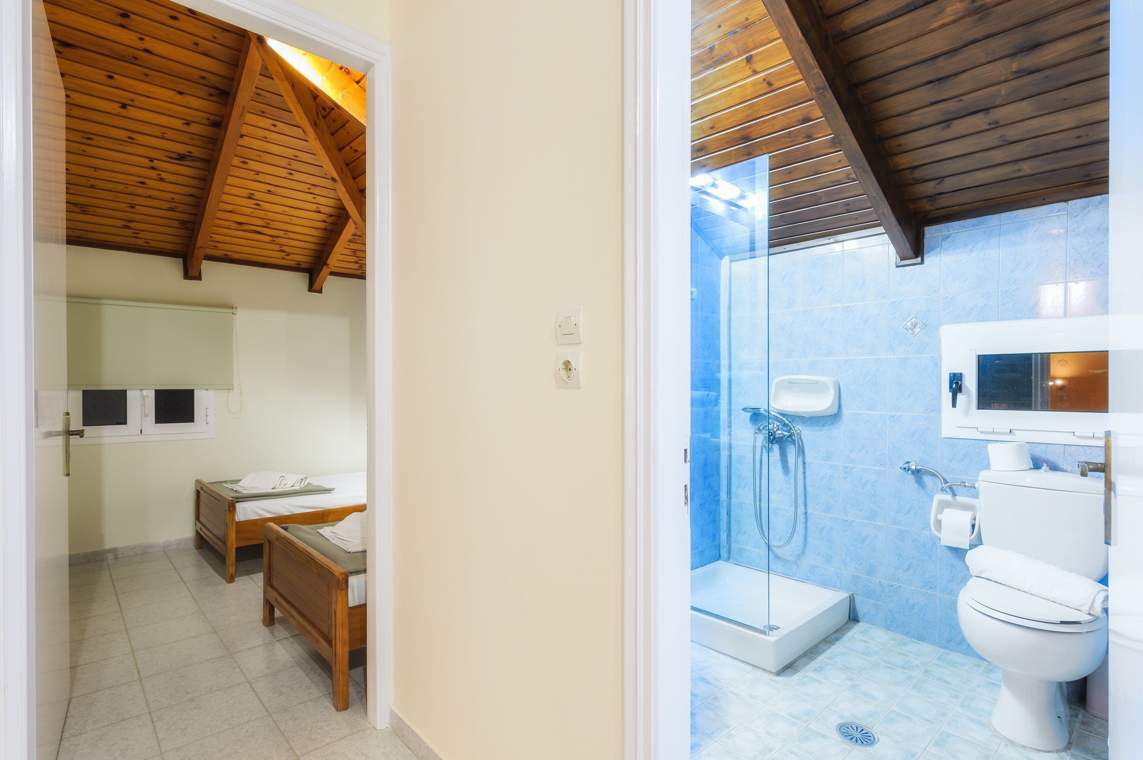 Una habitación con dos camas de madera, un baño pequeño con ducha y un inodoro.