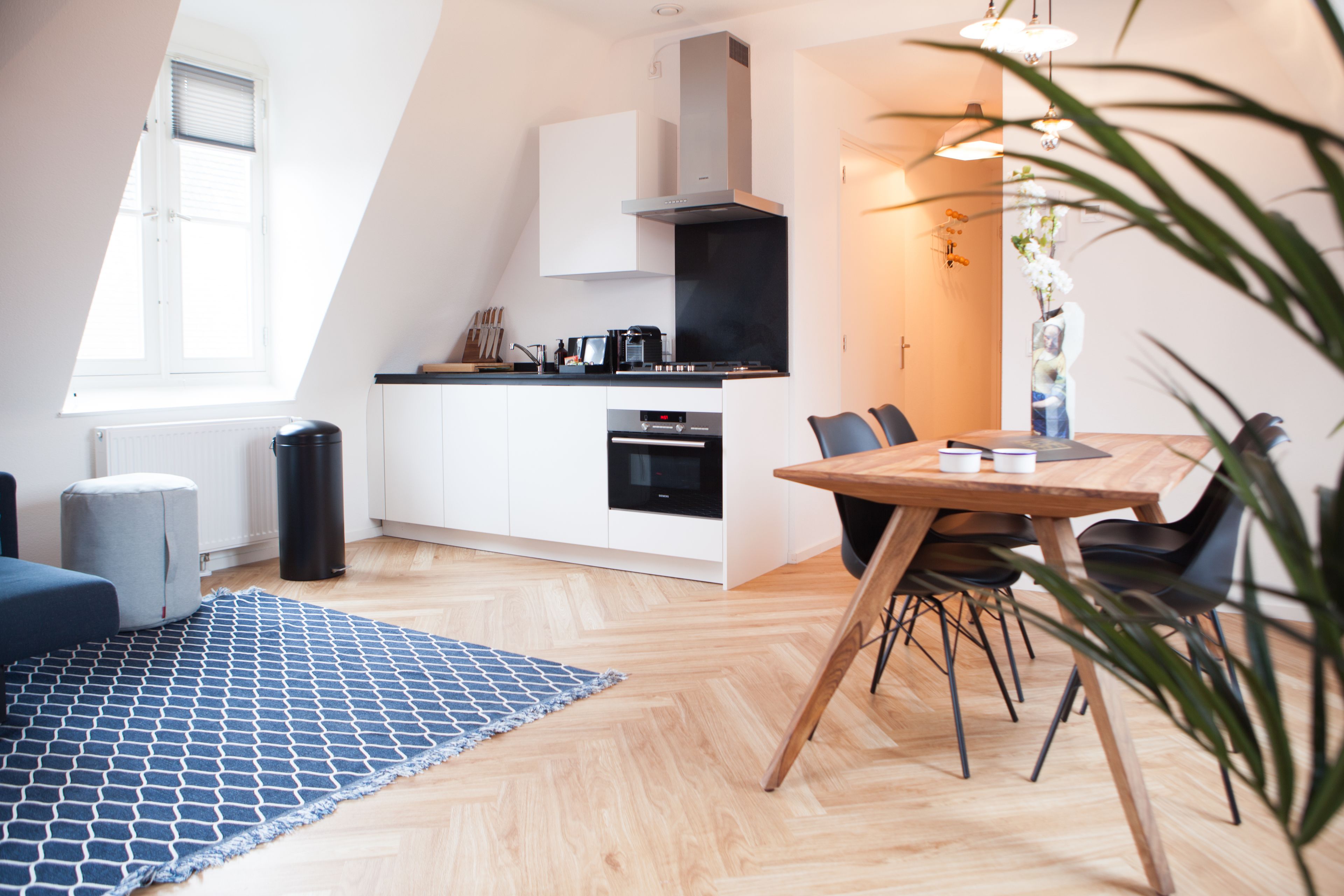 Una cocina moderna con armarios blancos, una estufa negra y un comedor con mesa y sillas de madera.