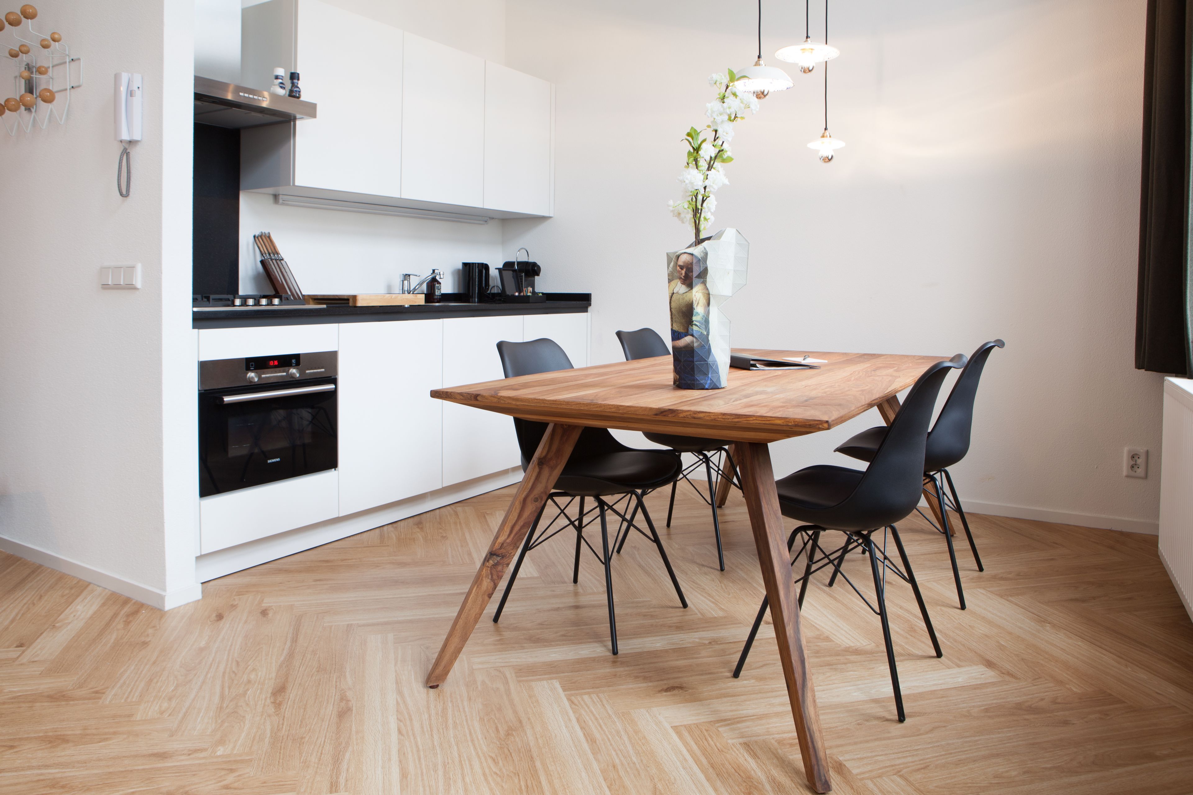 A modern kitchen with white cabinets, a wooden dining table, and black chairs.