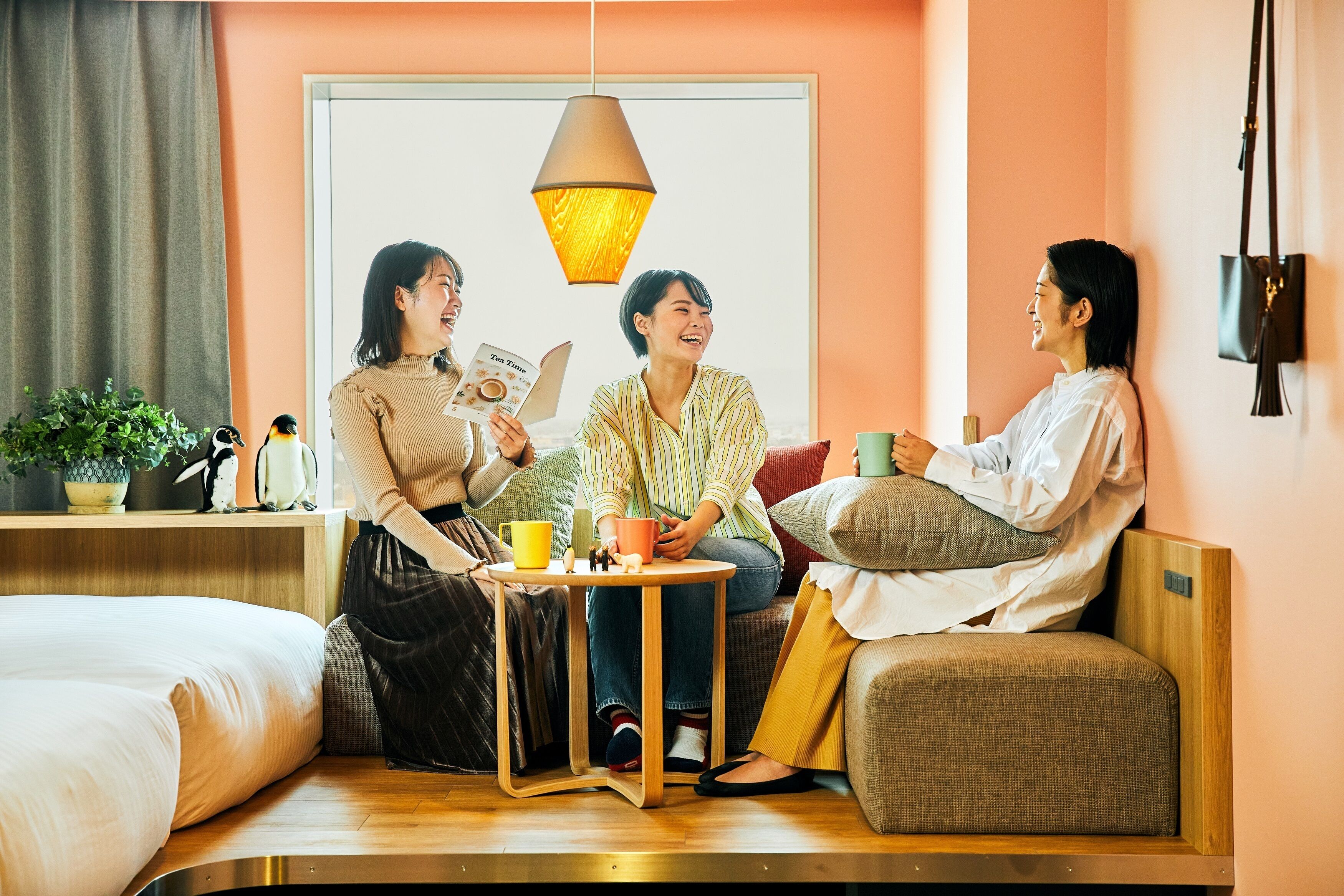 A cozy room with a sofa, a small table with cups and a book, and a hanging lamp.