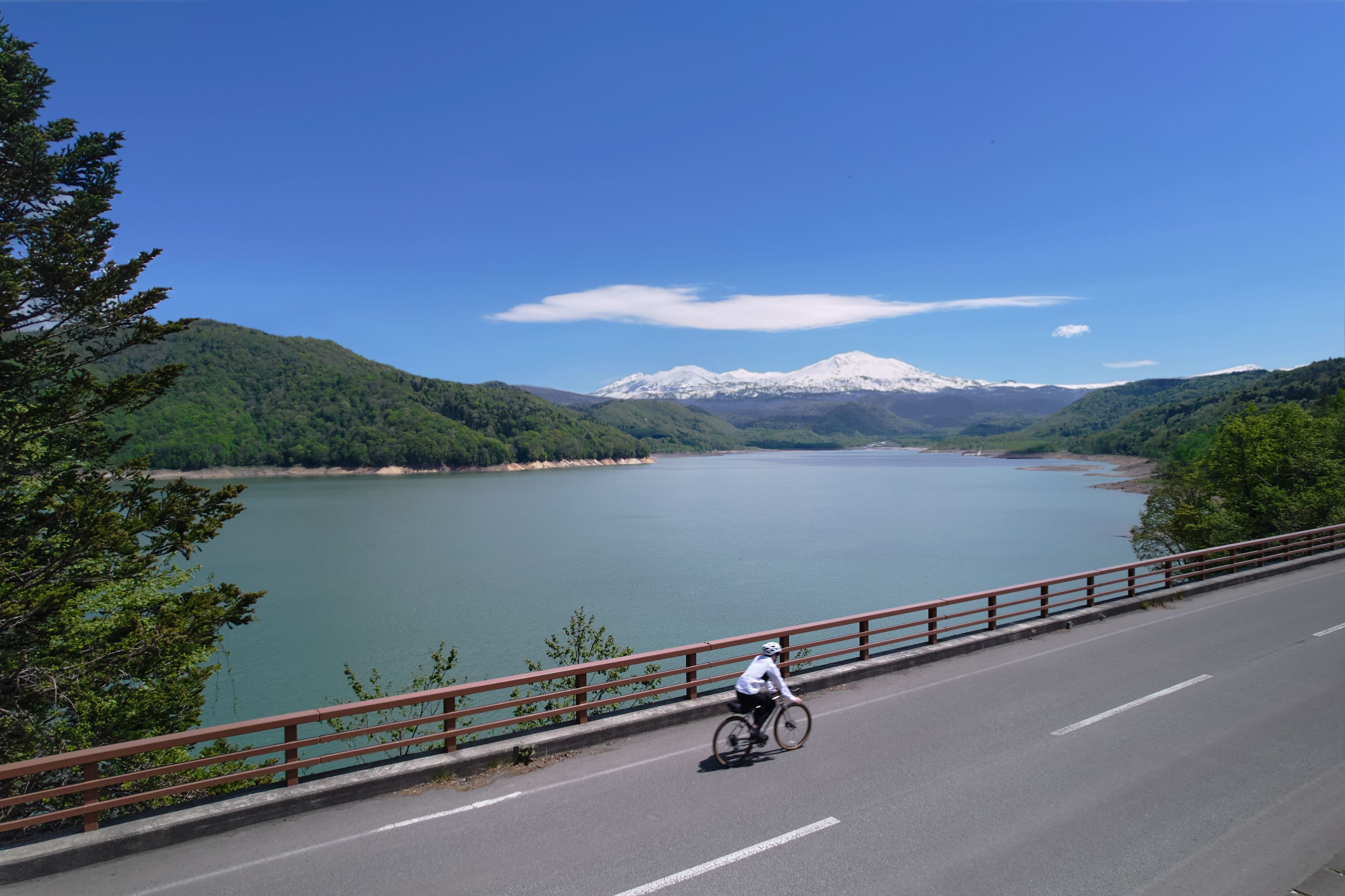 Un cycliste sur un pont, avec vue sur un lac et des montagnes.