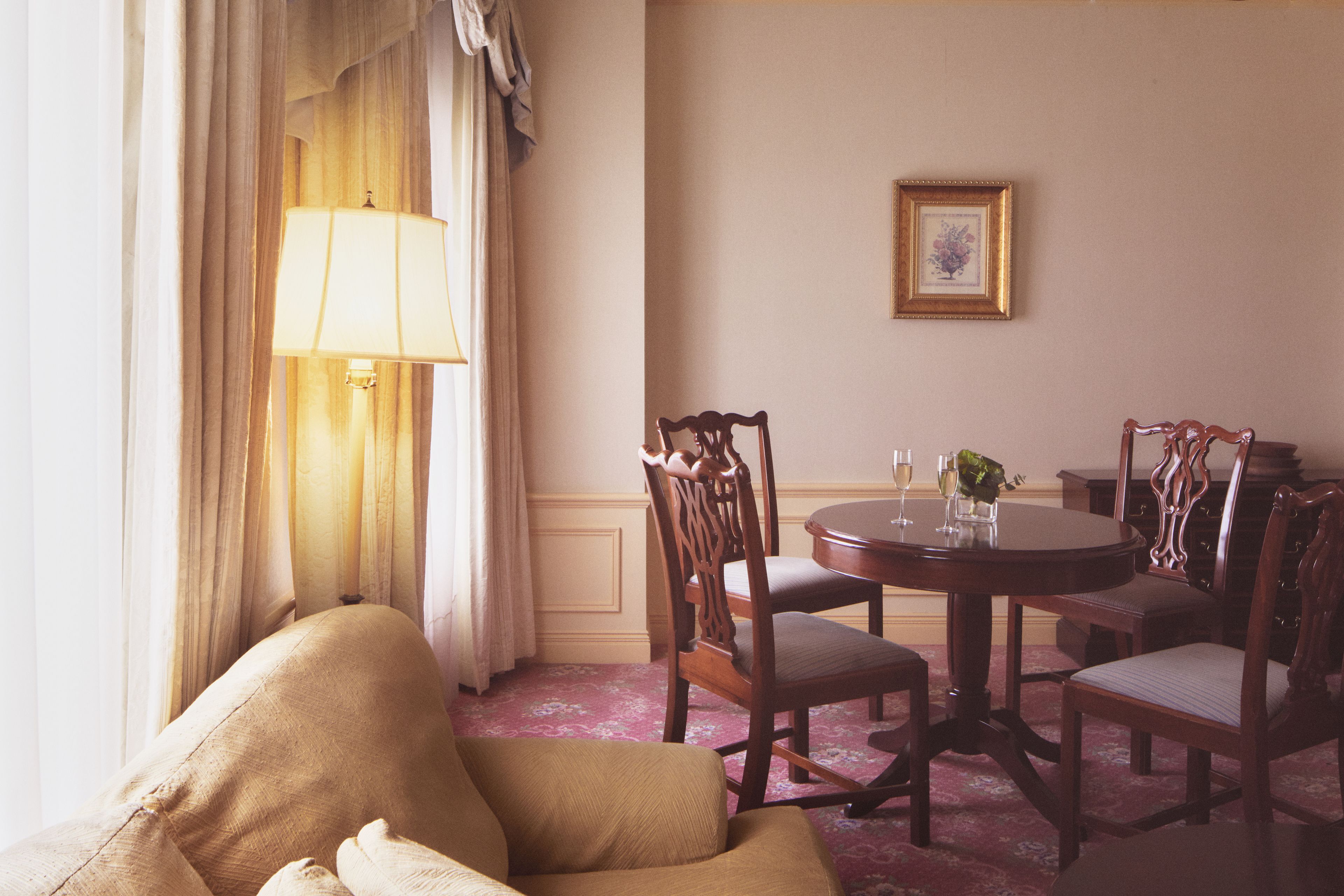 A dining area with a round table, four chairs, a lamp, and a framed picture on the wall.