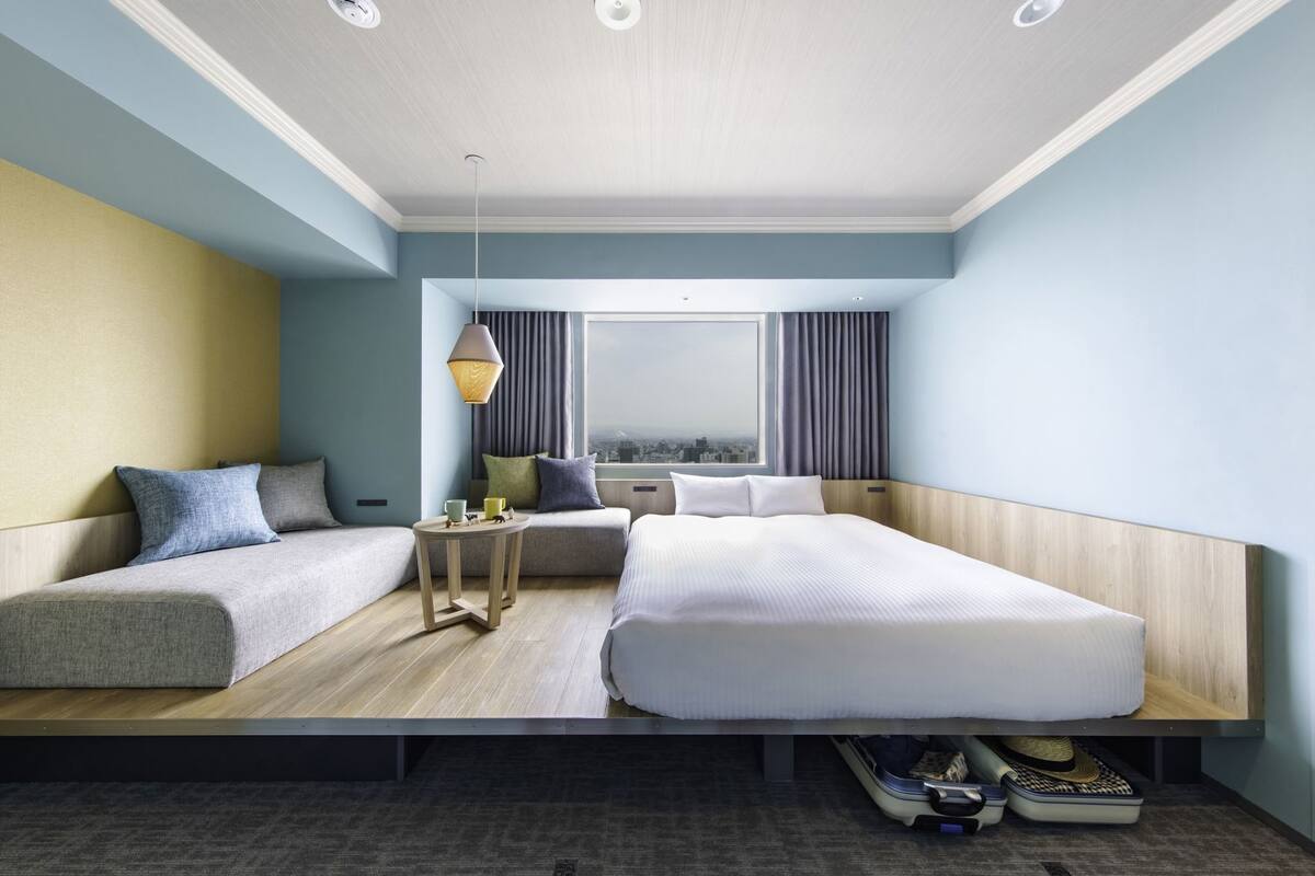 A modern hotel room with a bed, a sofa, a small table, and a view of the city.