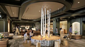 Een lobby met een centraal, rond zitgedeelte, omringd door houten krukken, een receptiebalie en een moderne kroonluchter.