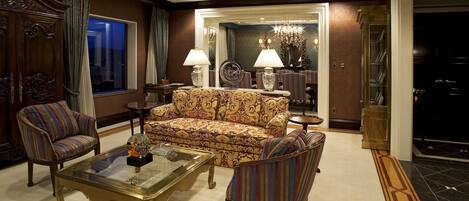 A spacious living room with a patterned sofa, striped armchairs, and a glass coffee table.