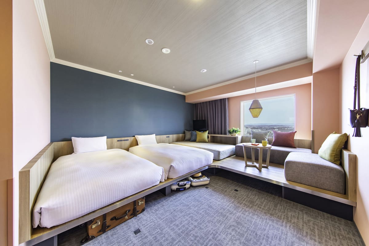 A modern hotel room with a large bed, a sofa, a small table, and a view of the city.