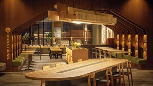 Een modern restaurant met een houten tafel in het midden, groene zachte zitplaatsen en een warme sfeer.