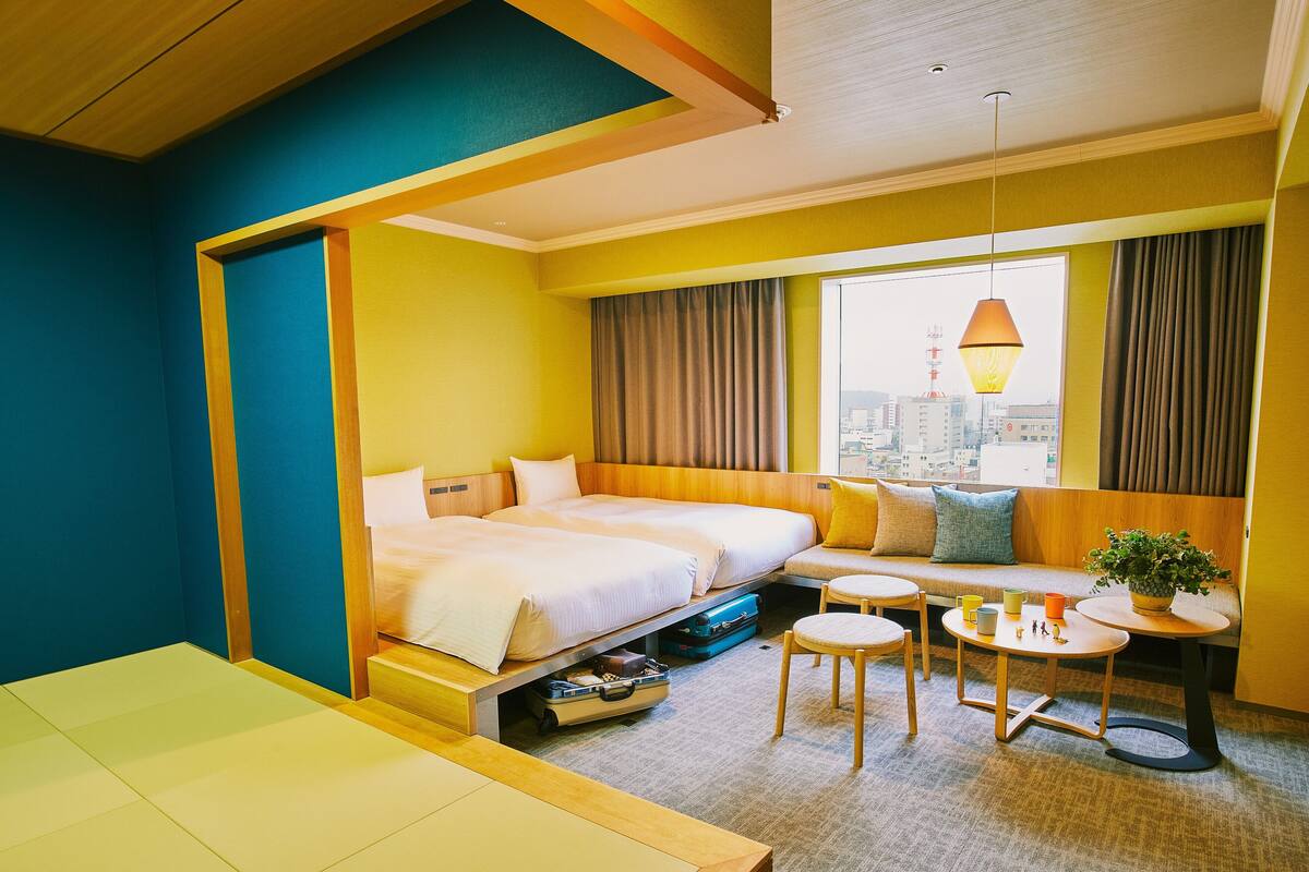 A hotel room with a bed, a sofa, a small table, and a view of the city.