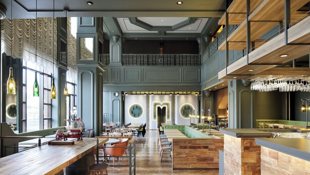 Een ruim restaurant in moderne stijl, met hoge plafonds, houten details en een centraal gelegen bar.