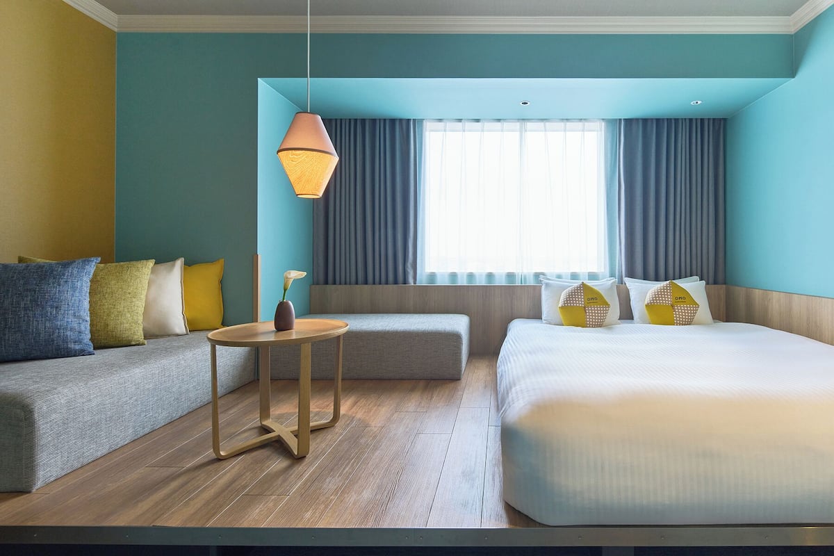 A hotel room with a bed, a sofa, a small table, and a hanging light fixture.