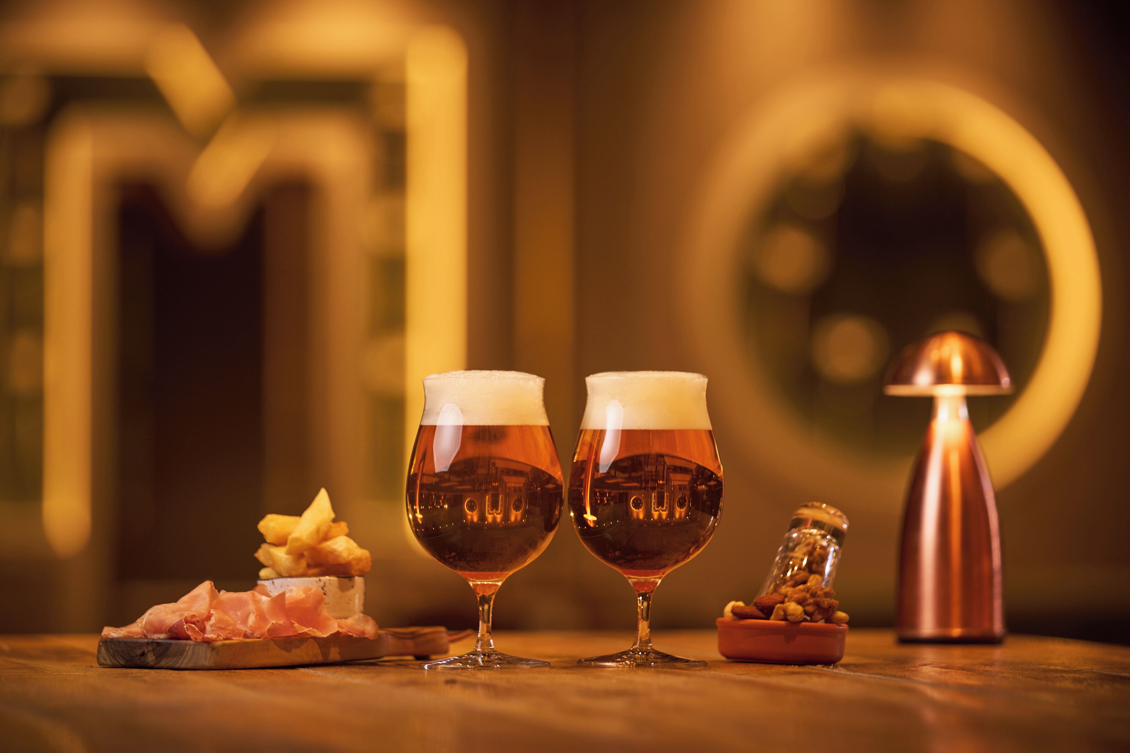 Two glasses of amber liquid, a glass jar, and a small dish with food on a wooden surface.