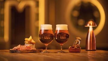 Two glasses of amber liquid, a glass jar, and a small dish with food on a wooden surface.