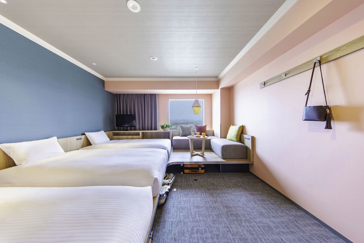 A hotel room with two beds, a sofa, a TV, and a view of the city.