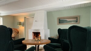 A cozy room with a fireplace, green upholstered chairs, a round wooden table, and a painting on the wall. - Husargårdens Bed & Breakfast (Sjobo)