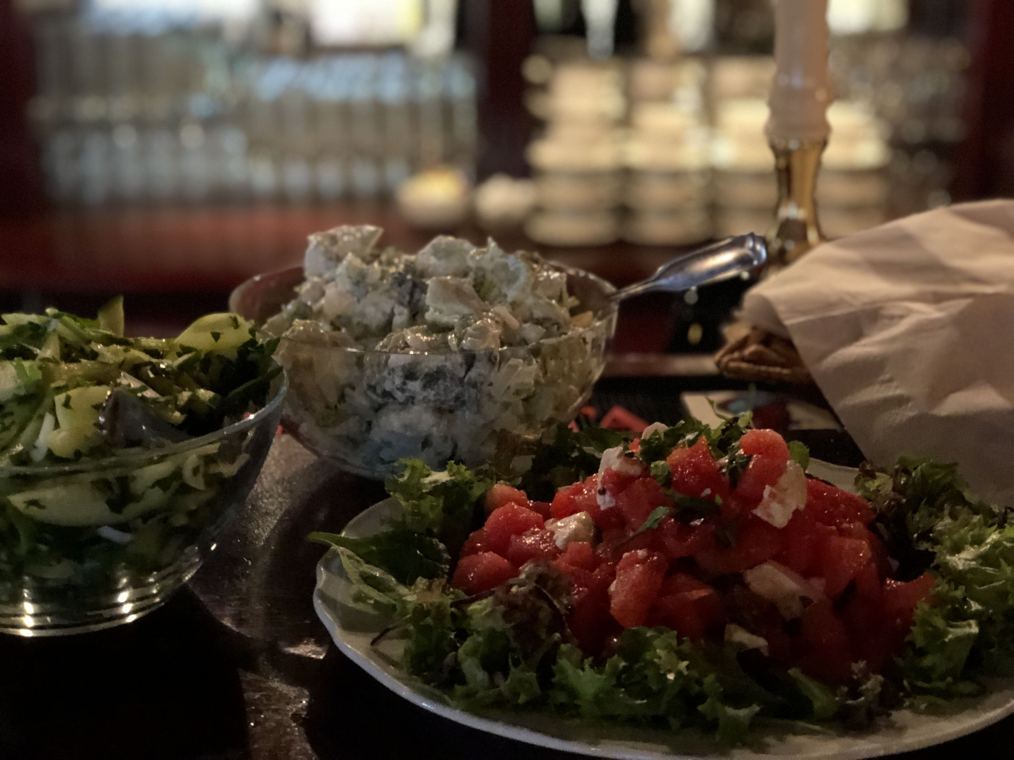 Un tavolo con diversi piatti, tra cui un'insalata, una ciotola di salsa gorgonzola e un piatto di pomodori a cubetti.