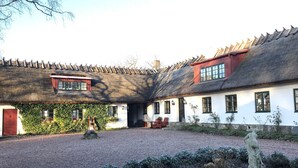 A traditional building with a thatched roof, a small wooden structure, and a gravel courtyard. - Husargårdens Bed & Breakfast (Sjobo)