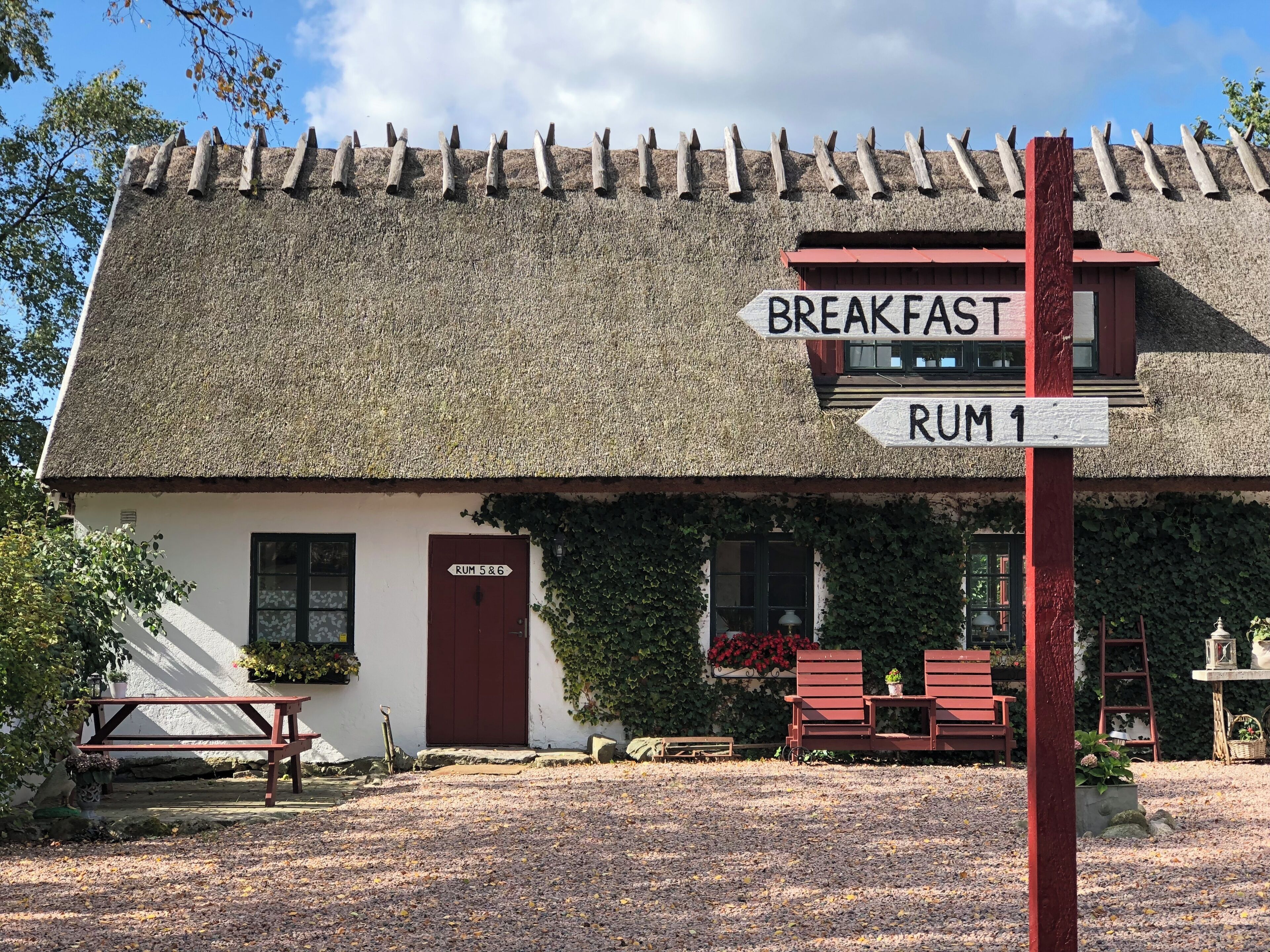 Un bâtiment rustique avec un toit de chaume, une enseigne indiquant l’emplacement du coin petit-déjeuner et une porte portant l’inscription « Rum 5 et 6 ».