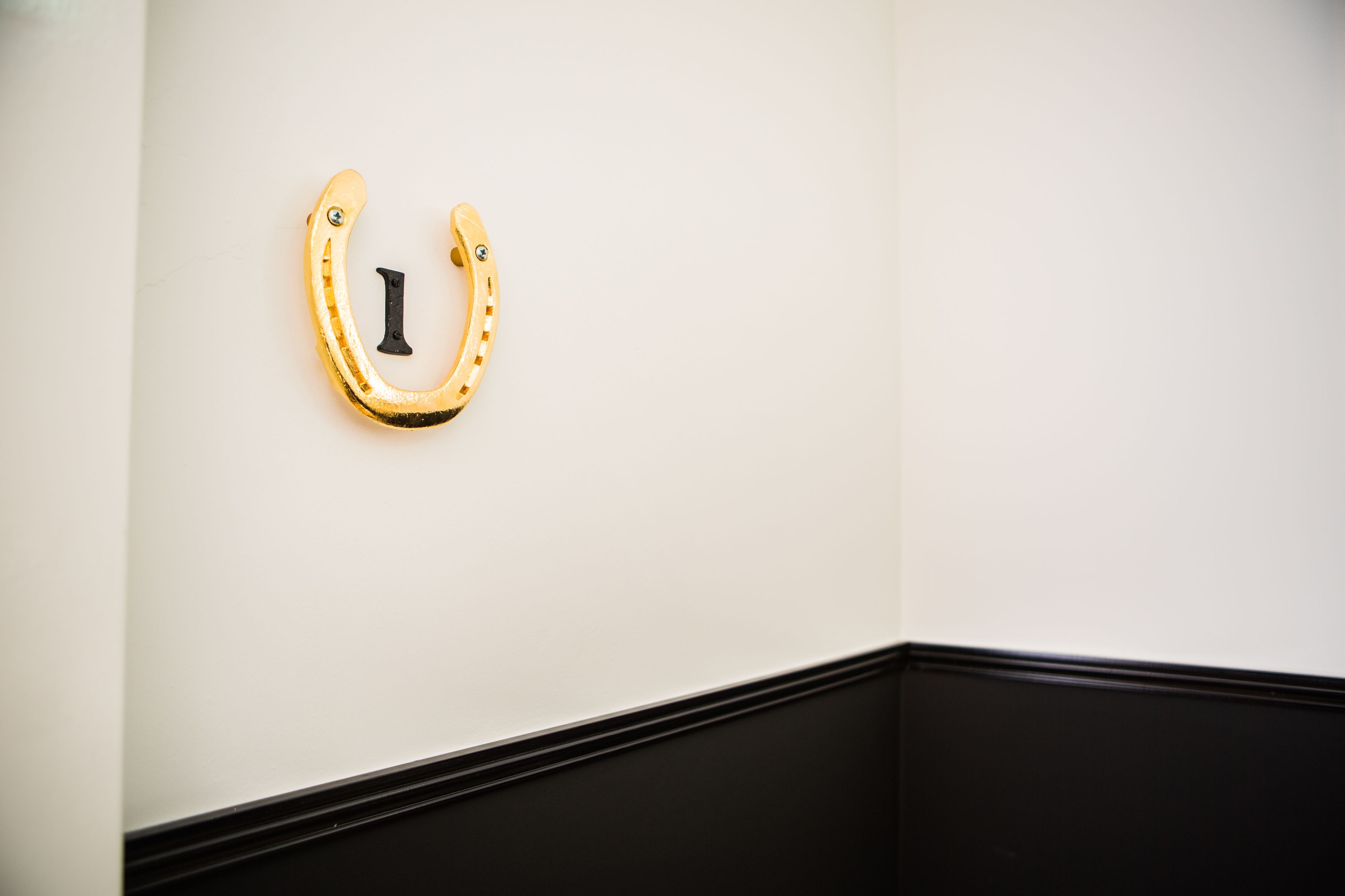 Un panneau mural en forme de fer à cheval, avec une lettre « I » majuscule au centre, fixé sur un mur blanc avec une plinthe noire.