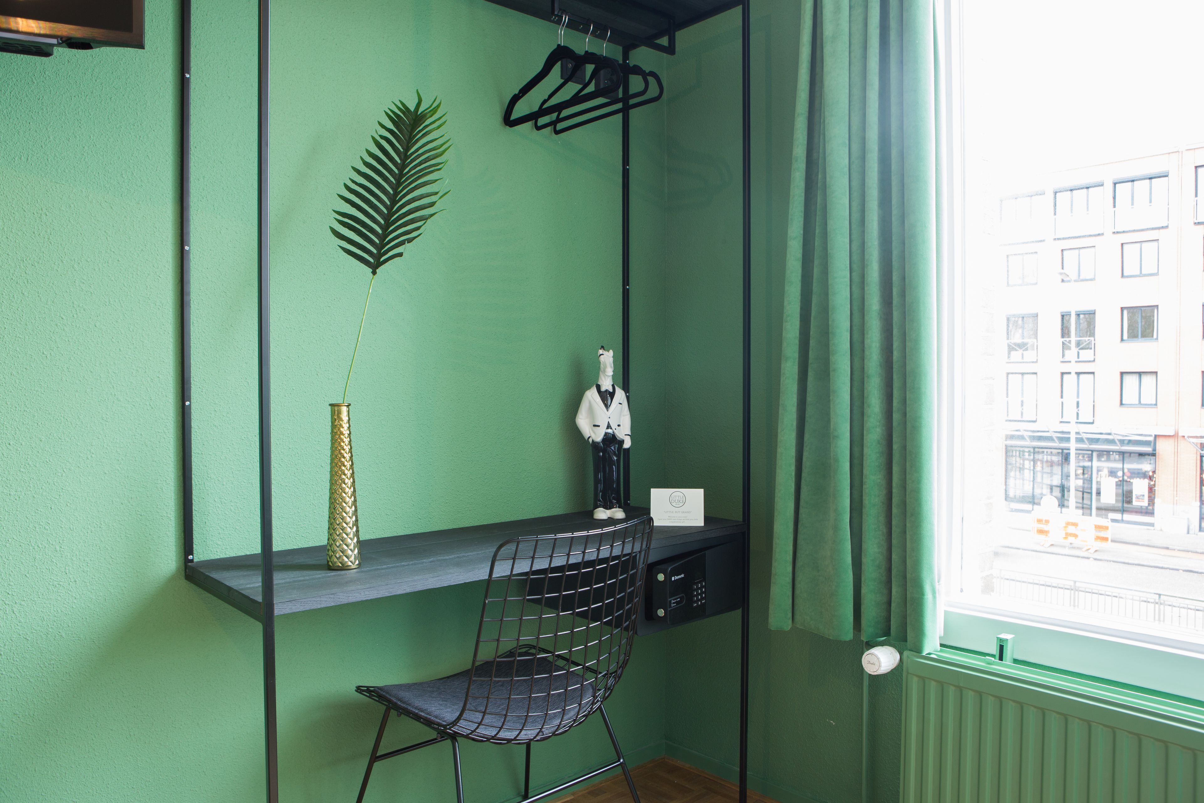 A room with a green wall, a desk with a chair, a hanging plant, and a window with curtains.