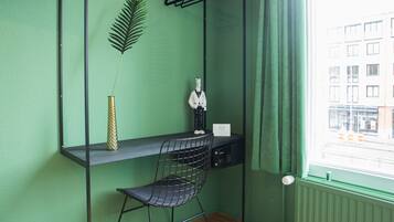 A room with a green wall, a desk with a chair, a hanging plant, and a window with curtains.