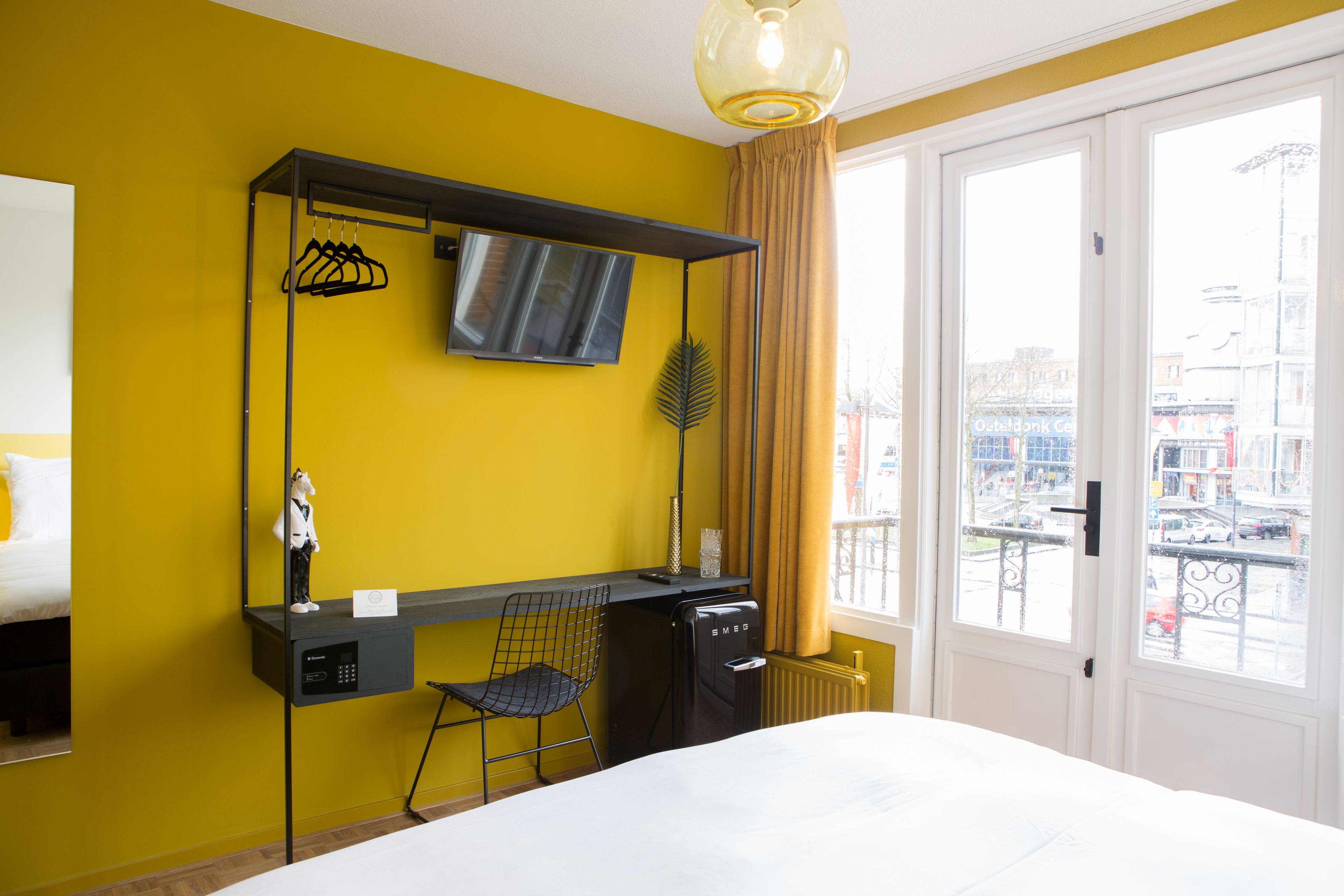Une chambre d’hôtel avec un lit, un bureau et une chaise, une télévision et une fenêtre avec des rideaux.