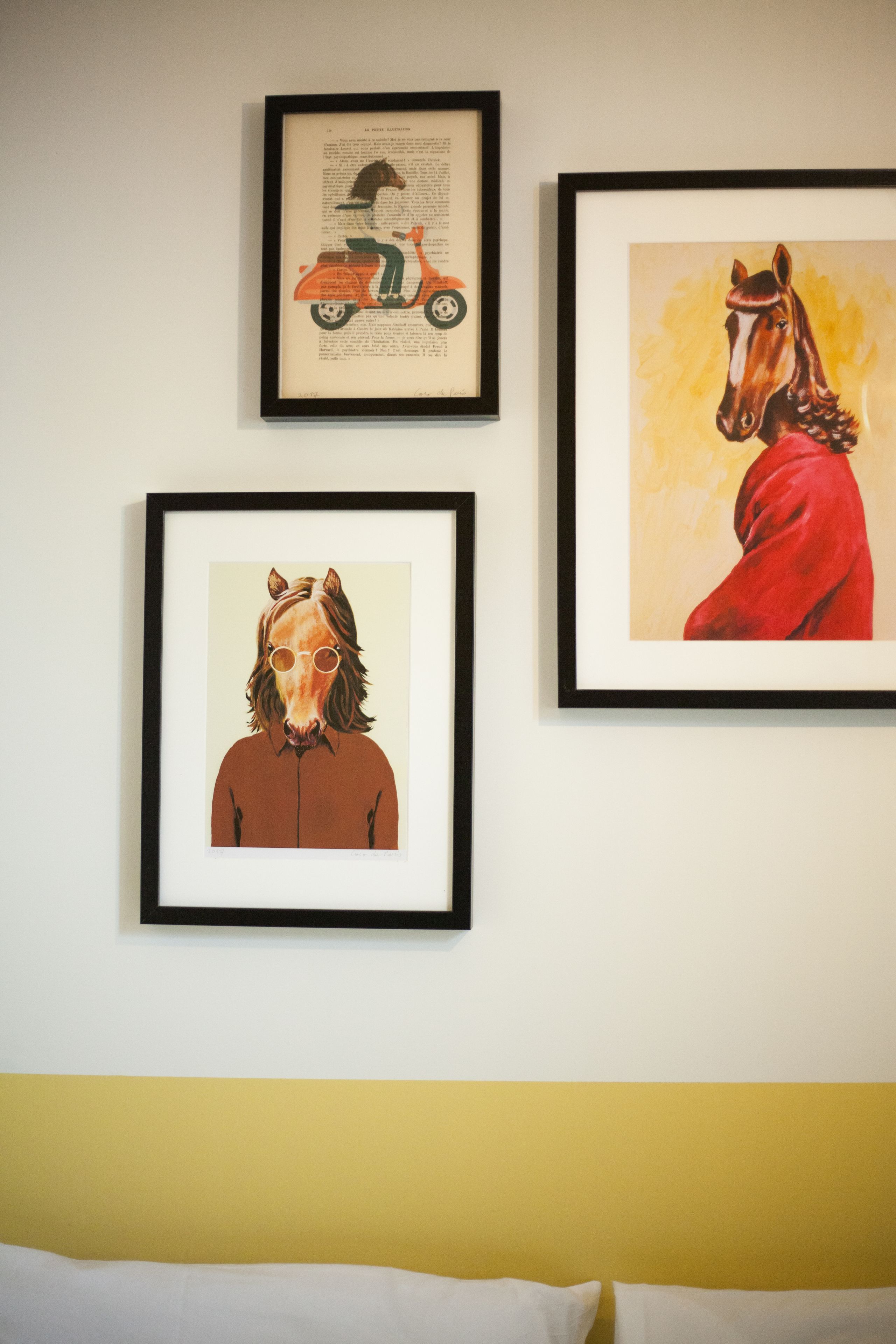 Three framed artworks on a wall above a bed.