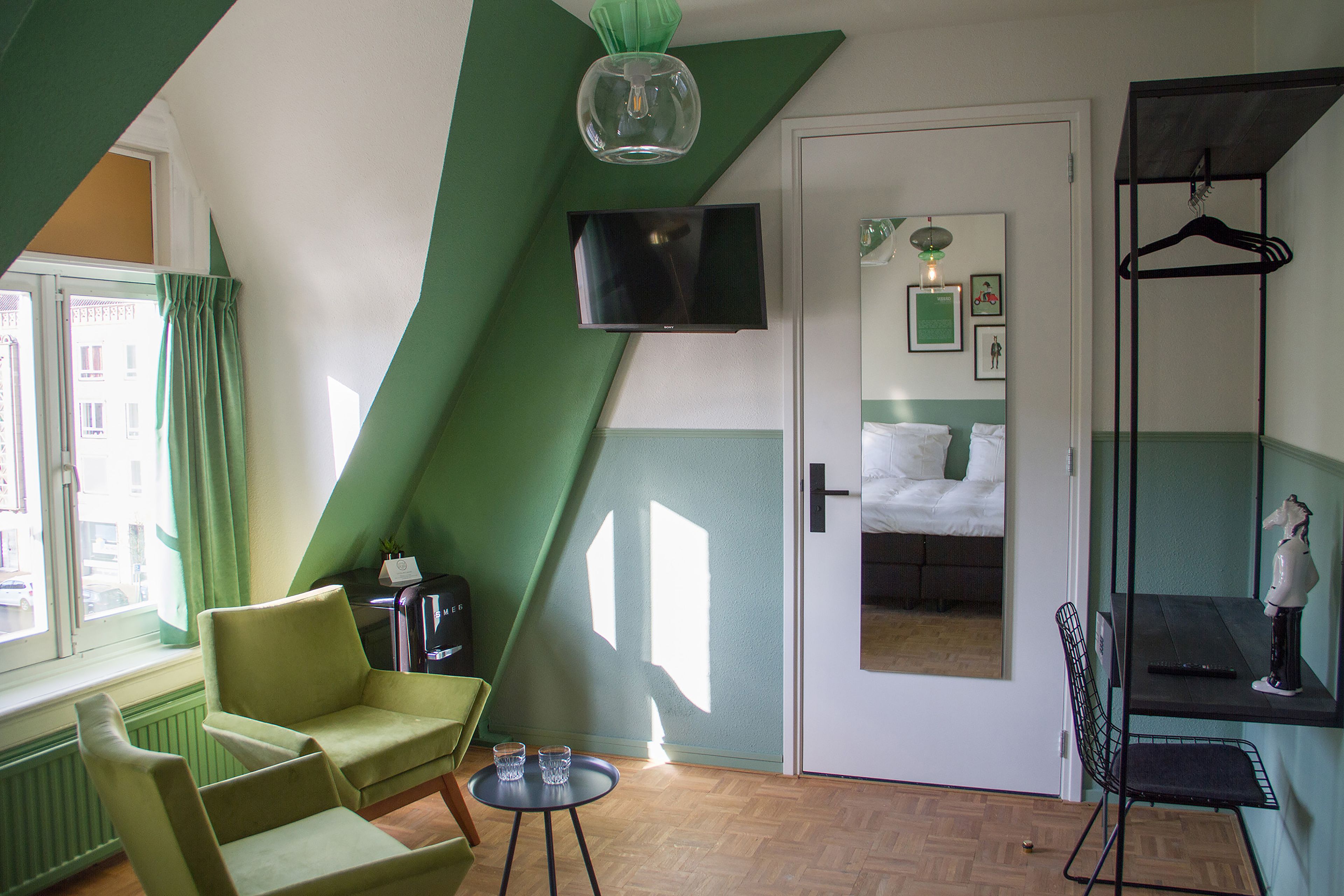 Una habitación con cama, televisor, silla, mesa y perchero.