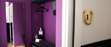 A room with purple walls, a black dresser, a mirror, a black hanger, and a gold horseshoe-shaped object on the wall.
