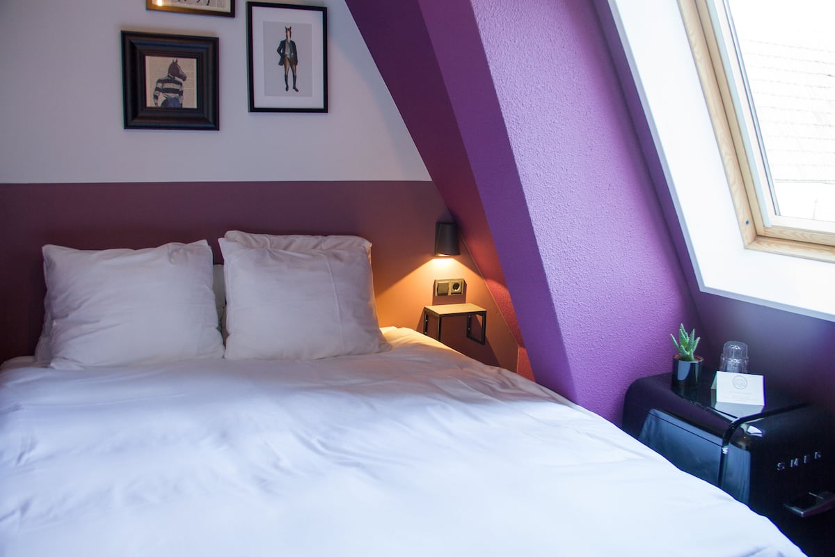 A bedroom with a bed, a nightstand, a lamp, and a window.