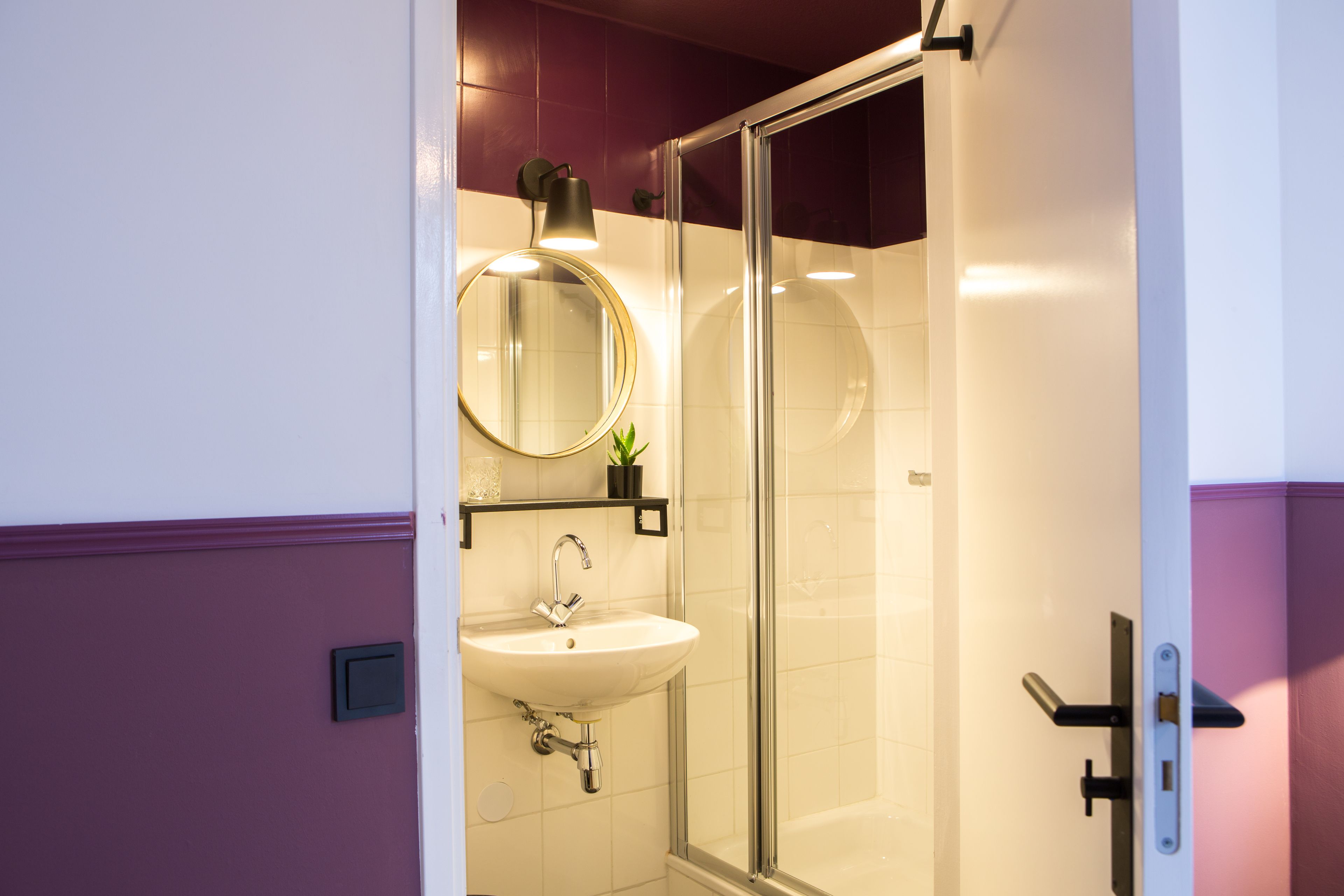 A bathroom with a glass shower enclosure, a round mirror, and a white sink.