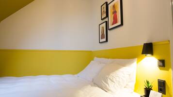 A neatly made bed with white linens, a bedside table with a lamp, and a small potted plant.