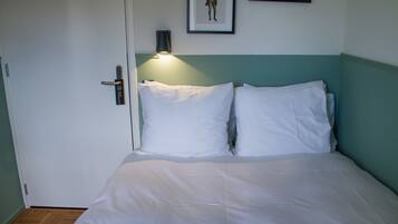 A bed with white bedding, a teal headboard, and a wall-mounted light fixture.