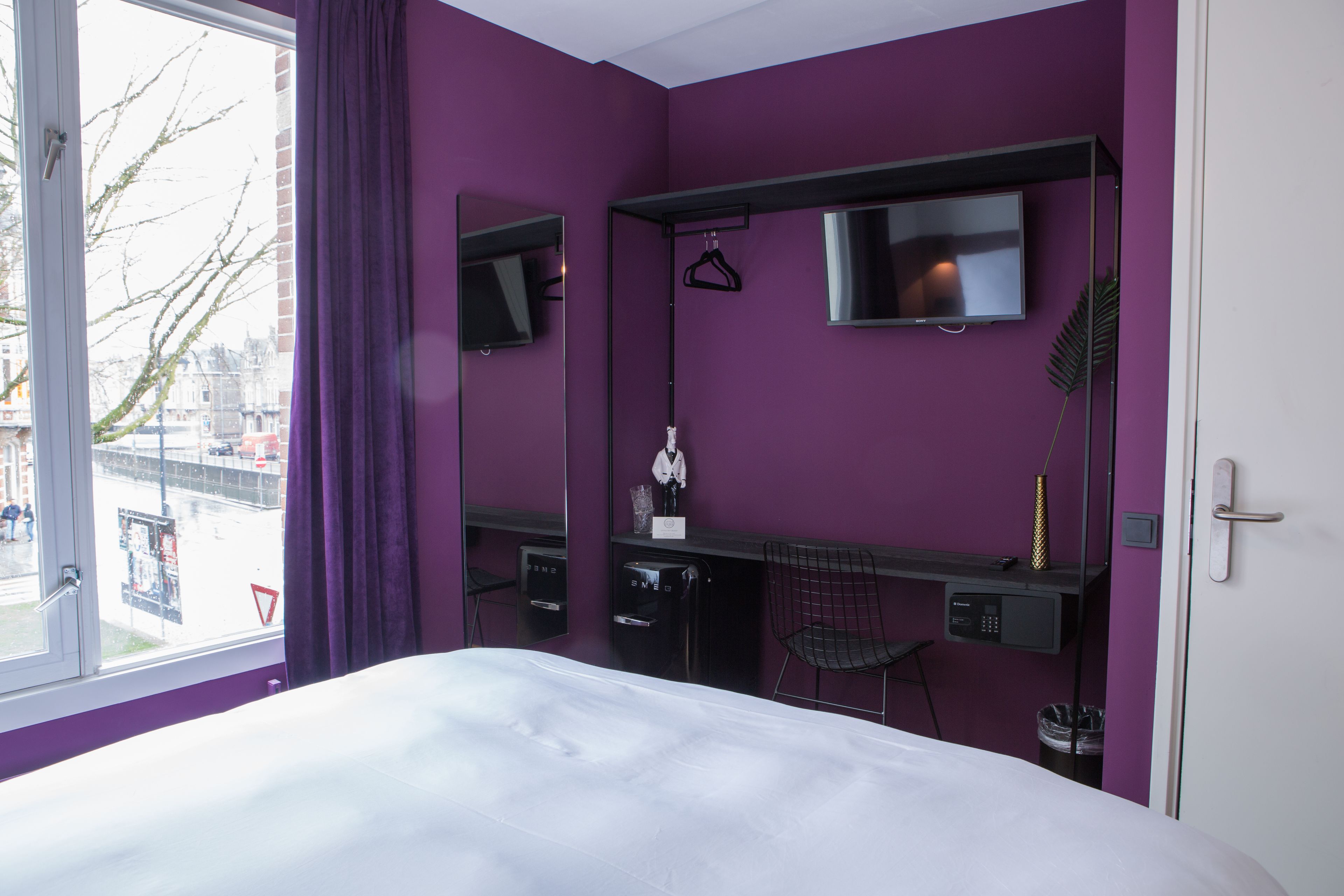 Camera d'albergo moderna con un letto grande, una scrivania con un computer, una televisione e una finestra con tende viola.