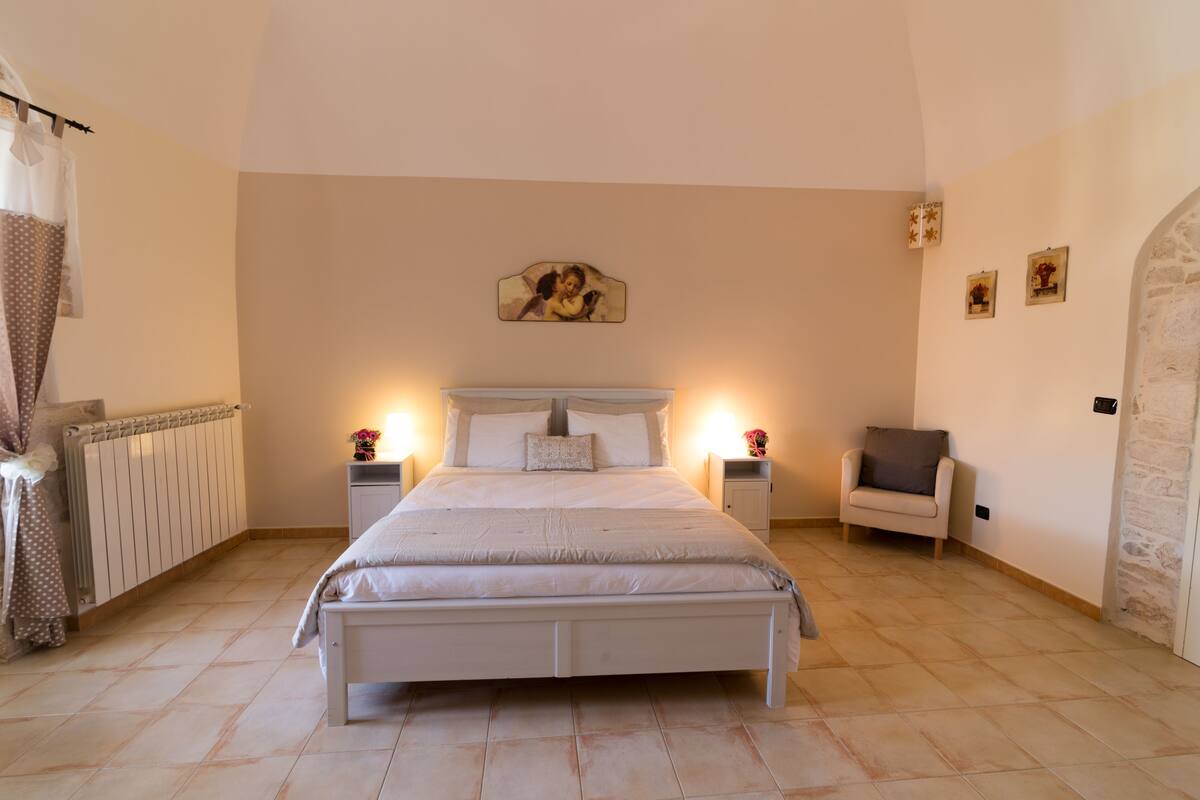 A bedroom with a large bed, two bedside tables with lamps, a chair, and a radiator.