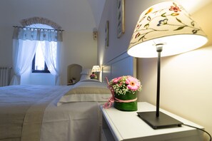 A neatly made bed with a white bedspread, a bedside lamp with a floral lampshade, and a vase of flowers on the nightstand. - B&B di Maria Chiara (Toritto)