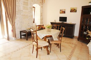 A dining area with a round table, chairs, a small side table, a cabinet, and a television. - B&B di Maria Chiara (Toritto)