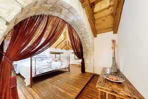 A bedroom with a stone archway, a wooden ceiling, a metal bed frame, and a small table with a decorative vase. - Villa Poseidon (Zakynthos)