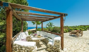 A stone patio with a wooden pergola, outdoor seating, and a view of the sea. - Villa Poseidon (Zakynthos)