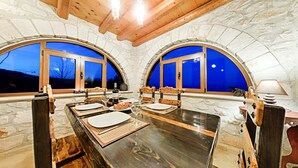 Zona pranzo con un lungo tavolo di legno, due finestre ad arco e pareti in pietra.
