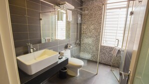 A modern bathroom with a large mirror, a white sink, a toilet, and a glass-enclosed shower area.