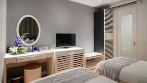A modern bedroom with a TV, a desk with a mirror, and two beds.