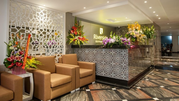 A reception area with a modern design, featuring a reception desk with floral arrangements, a patterned wall, and a seating area with brown sofas.