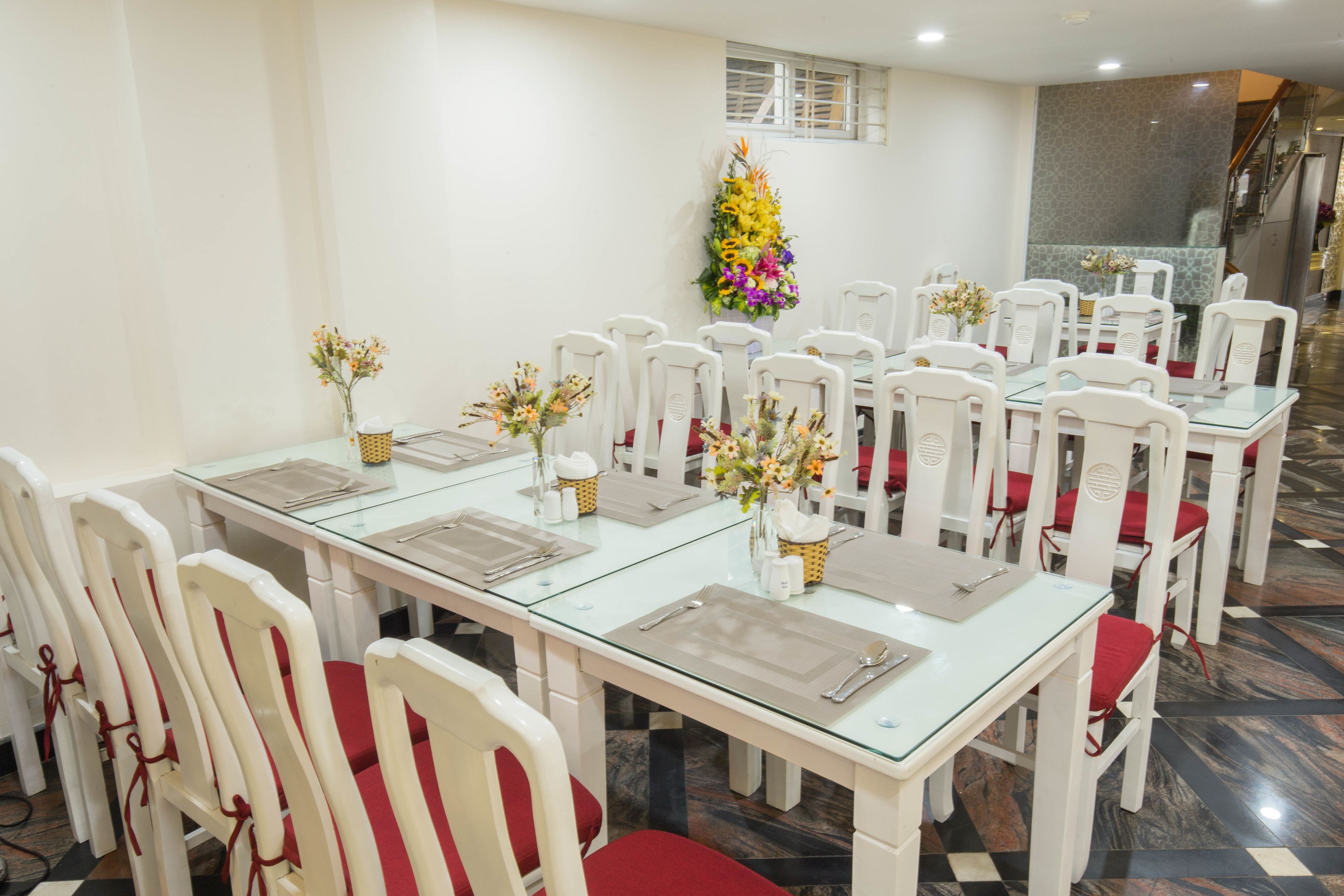 Un espace repas avec des chaises et des tables blanches, chaque table étant agrémentée d’un vase de fleurs et d’une serviette pliée.