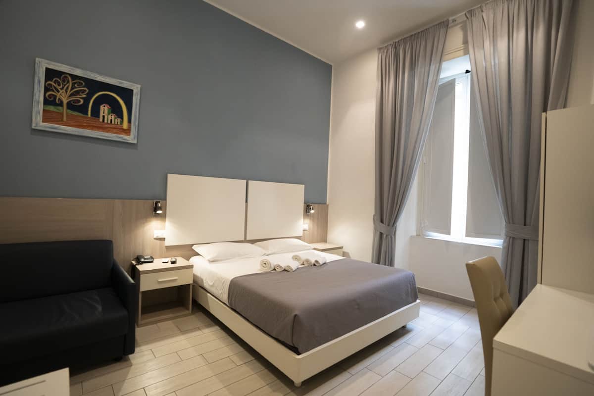 A modern hotel room with a bed, bedside tables, a desk, and a chair.